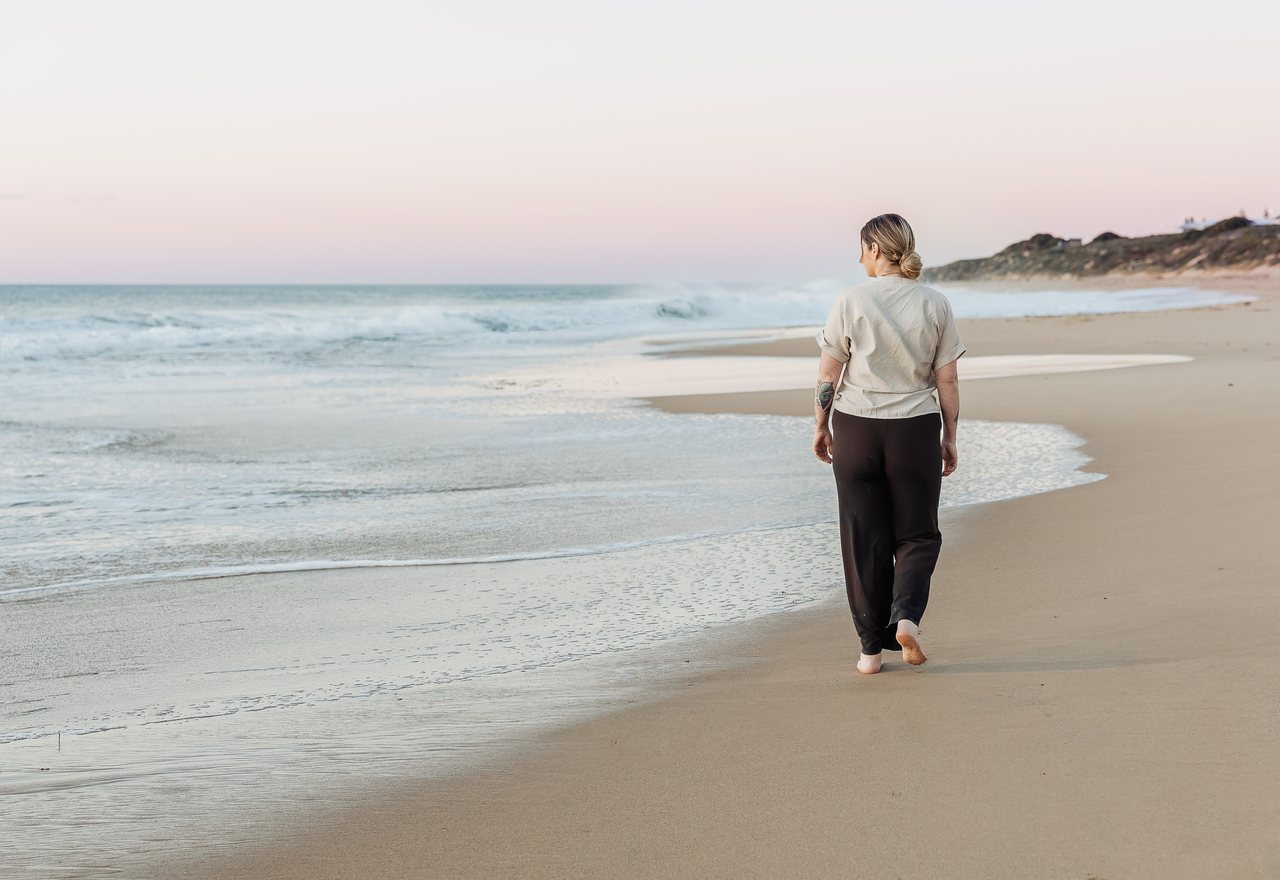 A woman walking barefoot along the shoreline at dusk.