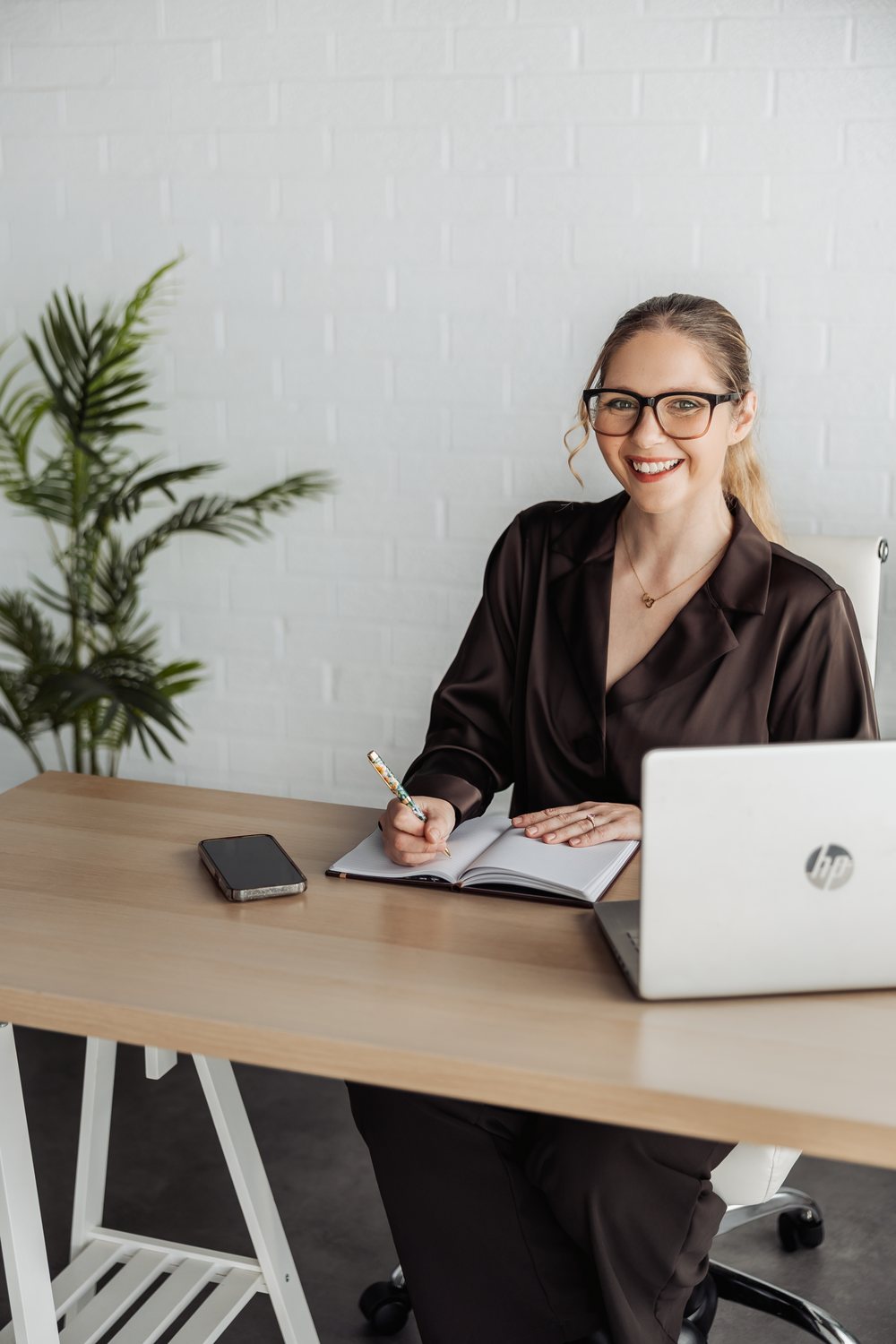 Tilly at her desk with a notebook and laptop, smiling.