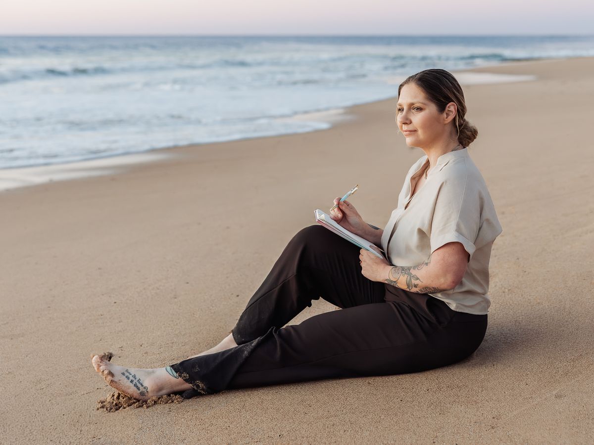 Tilly sitting on the beach at sunset, writing in a notebook